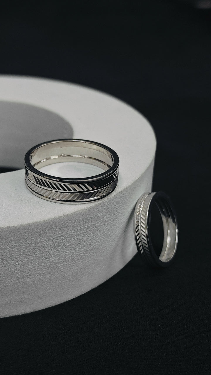 Silver rings with geometric designs on a white cylindrical object against a black background