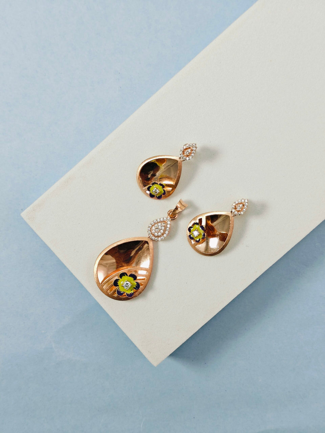 Rose gold earrings with green gemstones on a light gray card against a blue background