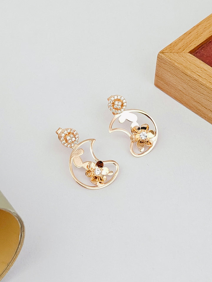 Gold earrings with floral designs on a light gray background