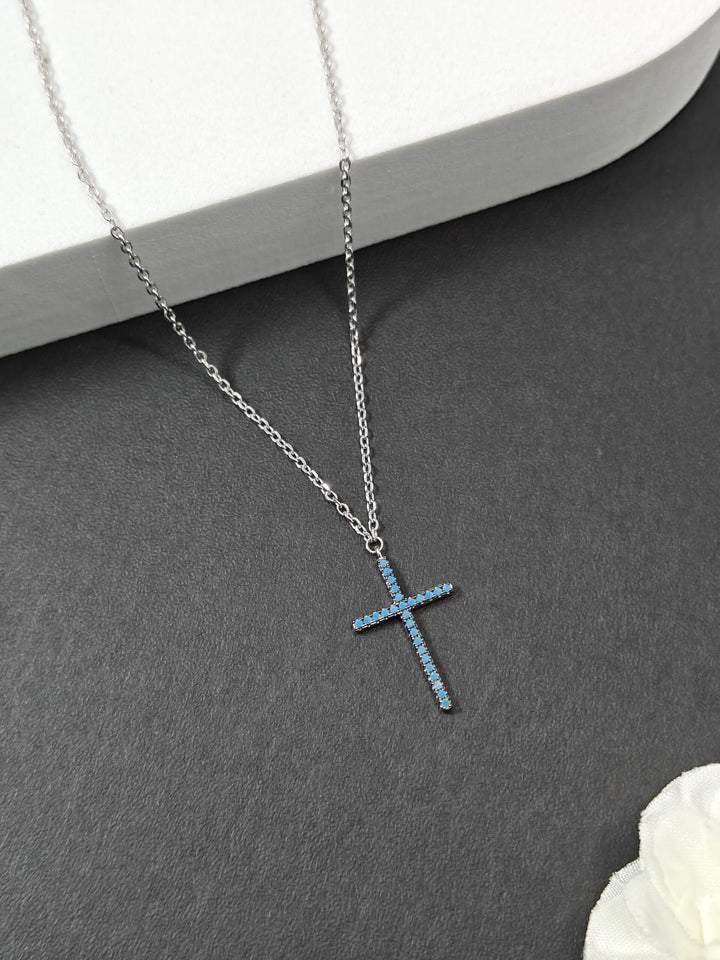Silver cross necklace on a gray surface with a white flower