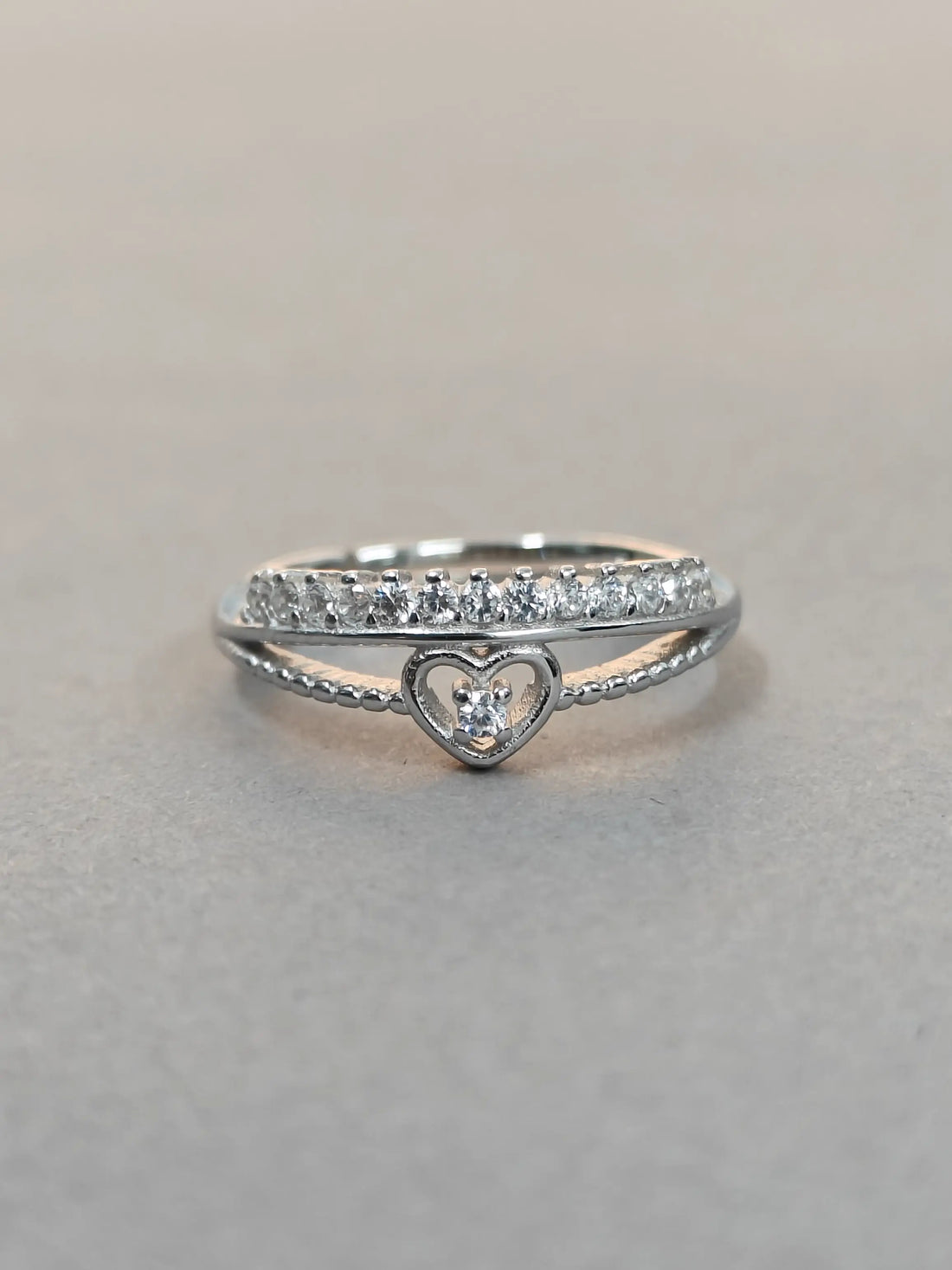 Silver ring with heart design and diamond accents on a gray background