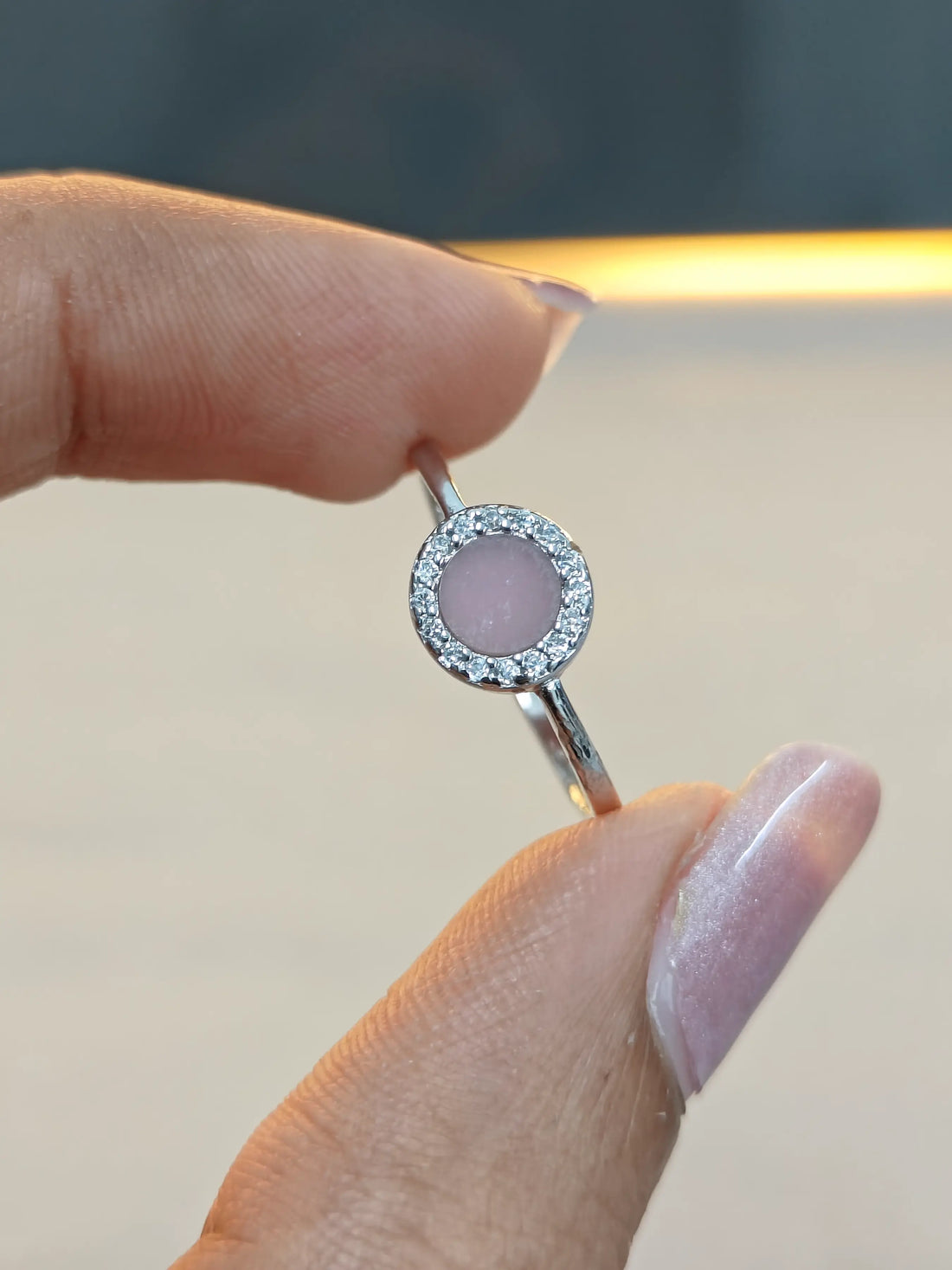 Silver ring with a pink gemstone held by a hand against a neutral background