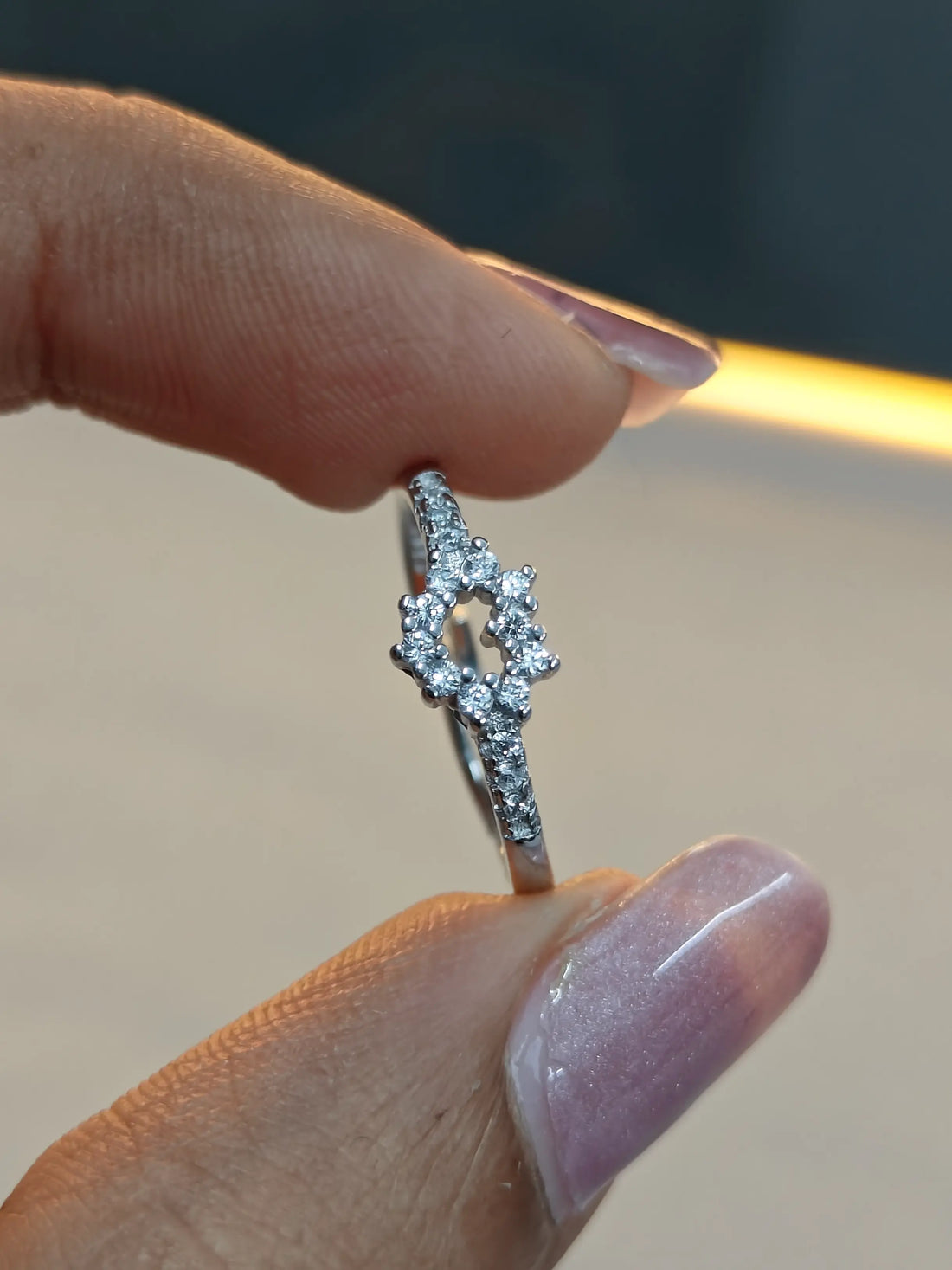 Silver ring with diamonds held between fingers against a blurred background