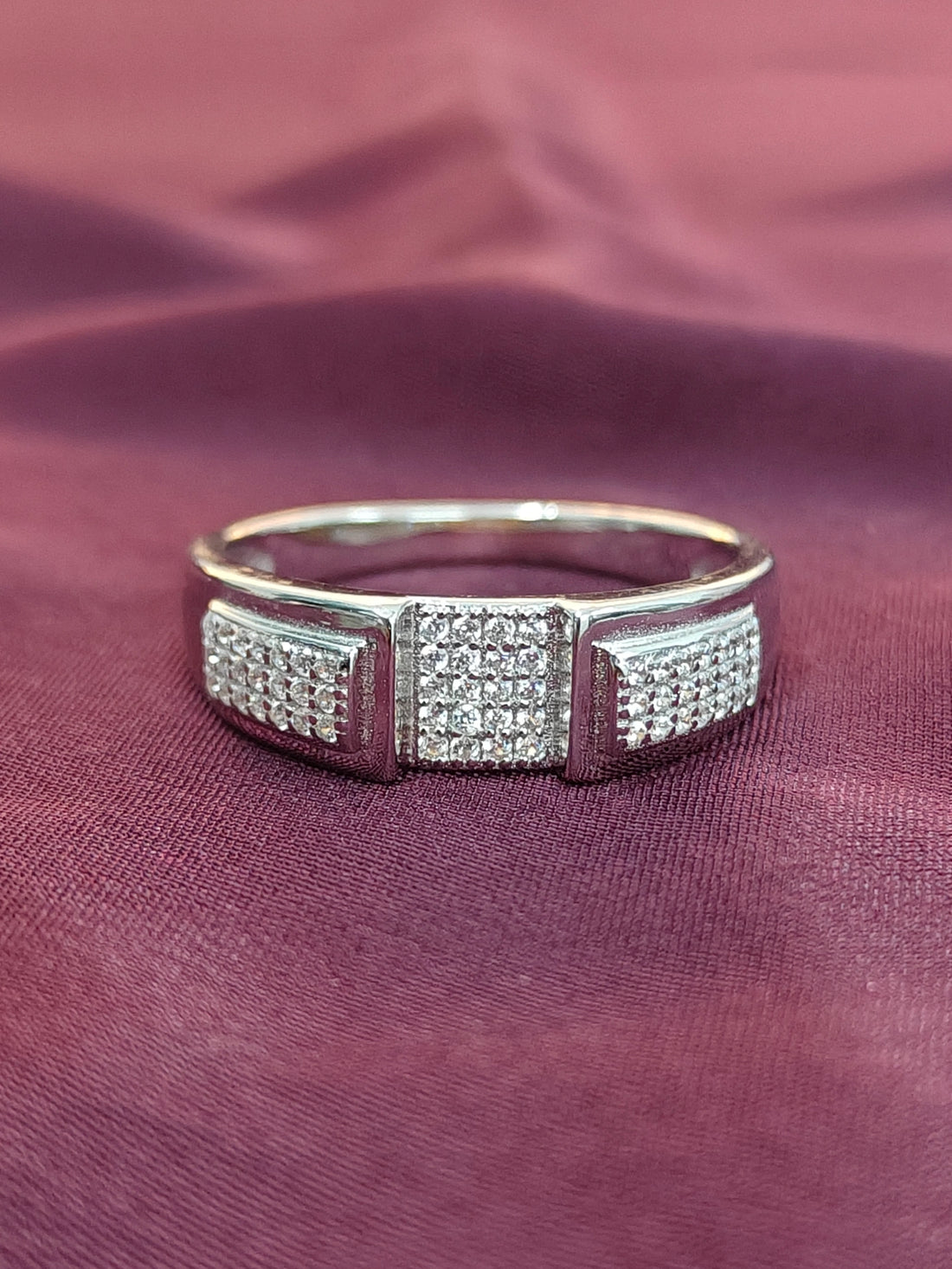 Silver ring with diamond accents on a maroon fabric background