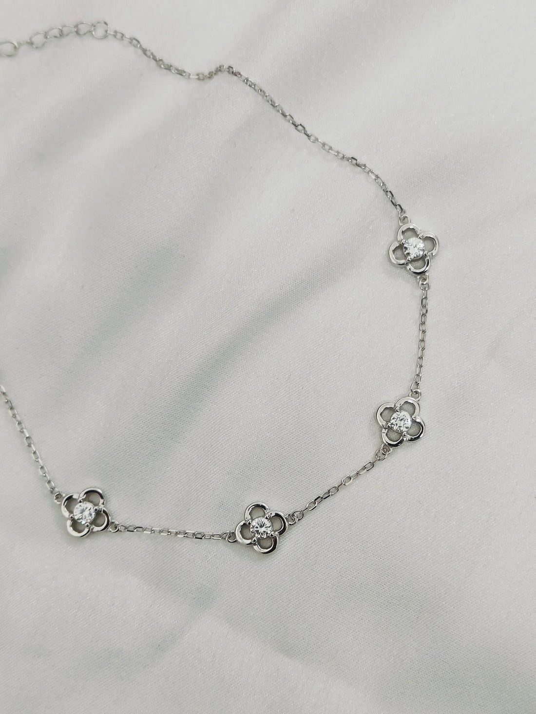 Silver necklace with flower-shaped pendants on a light gray background