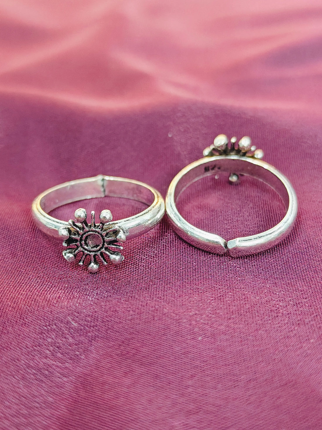Two silver rings with decorative elements on a pink fabric background