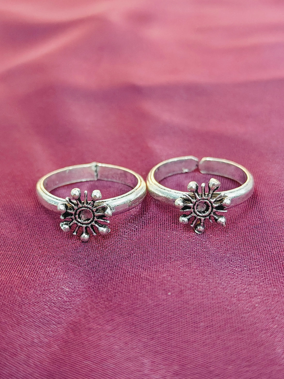 Two silver sun-shaped rings on a pink fabric background