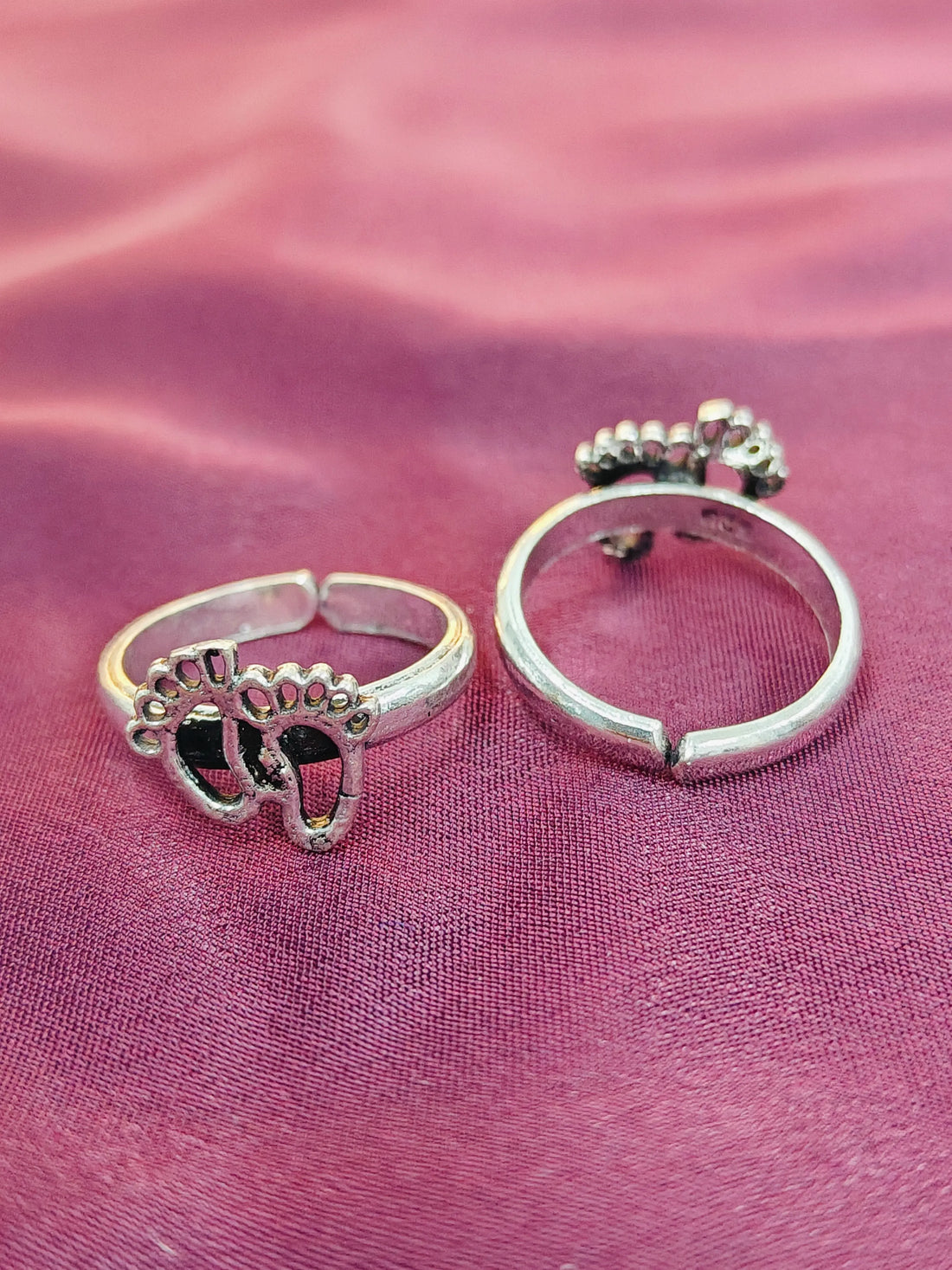 Two silver rings with paw print designs on a pink fabric background