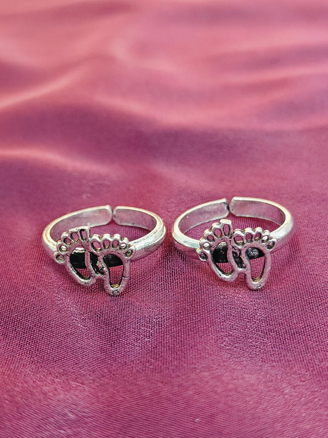 Two silver rings with paw print designs on a pink fabric background