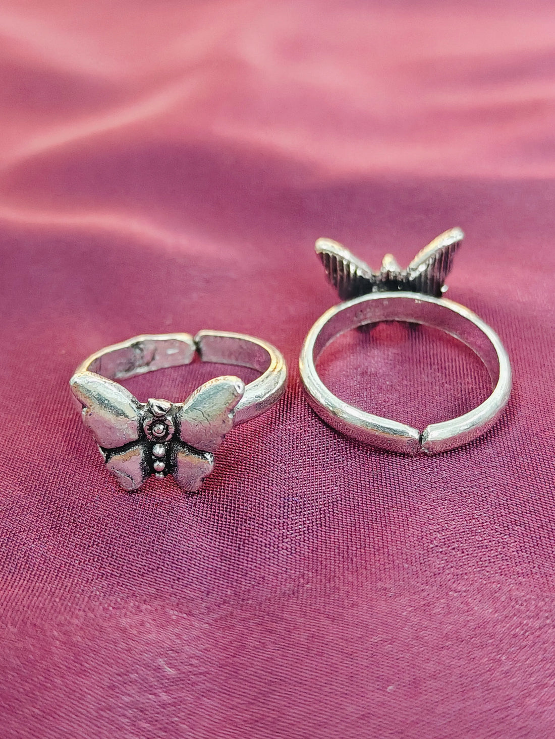 Two butterfly-shaped silver rings on a pink fabric background