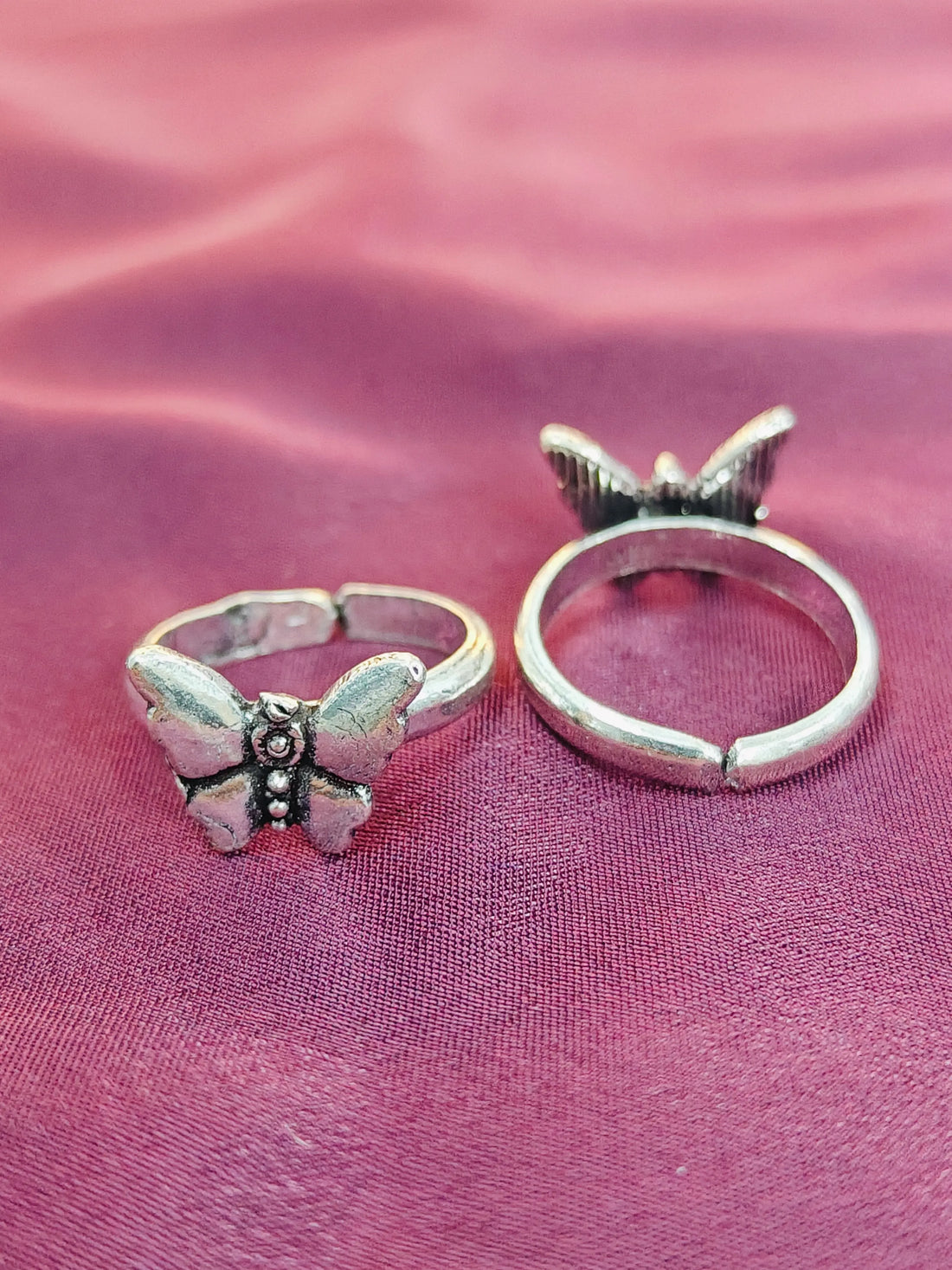 Two butterfly-shaped silver rings on a pink fabric background