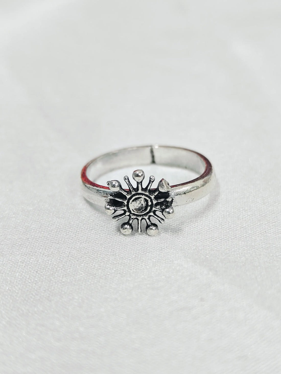 Silver ring with sun design on a light gray background
