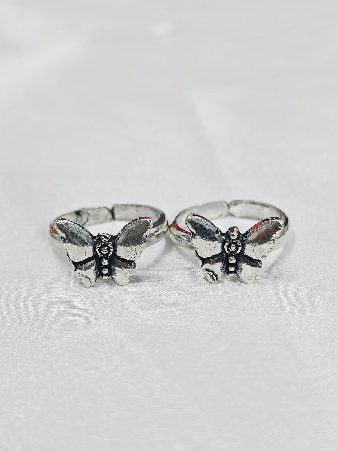 Two silver butterfly rings on a light gray background