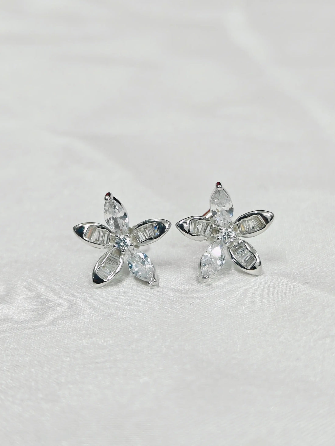 Silver flower-shaped earrings with clear gemstones on a light gray background