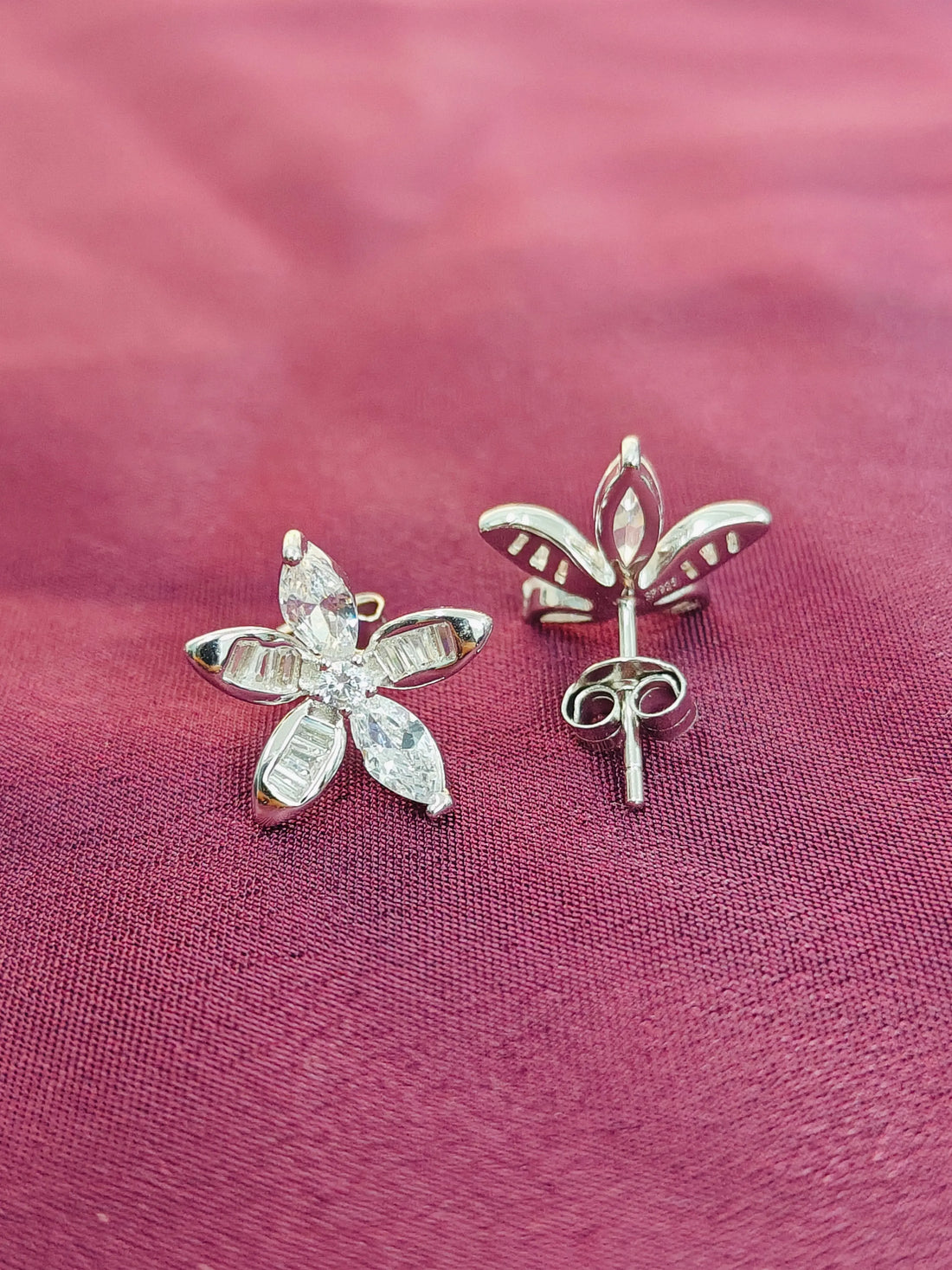 Silver flower-shaped earrings on a pink fabric background