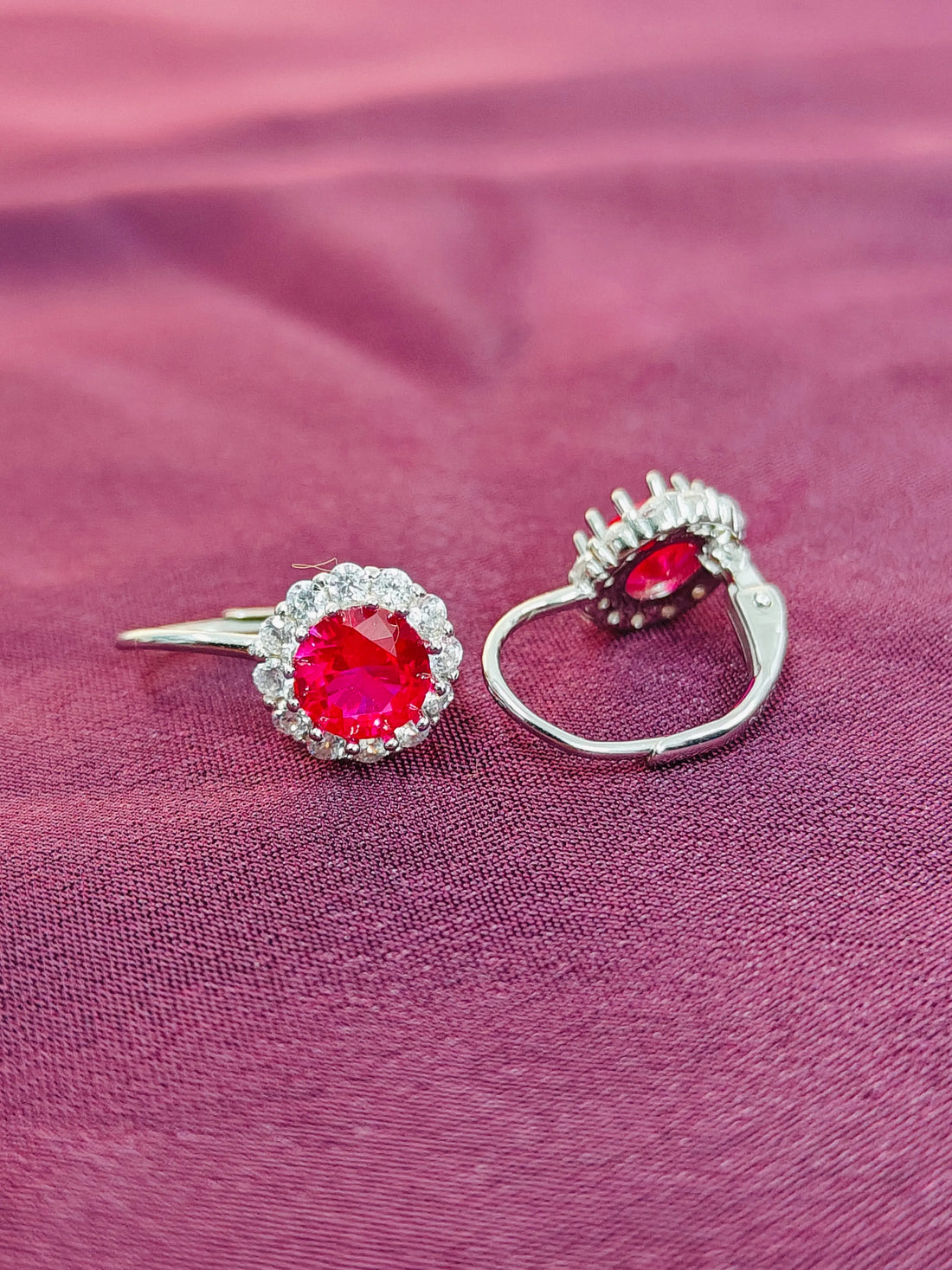 Pair of earrings with red gemstones on a pink fabric background