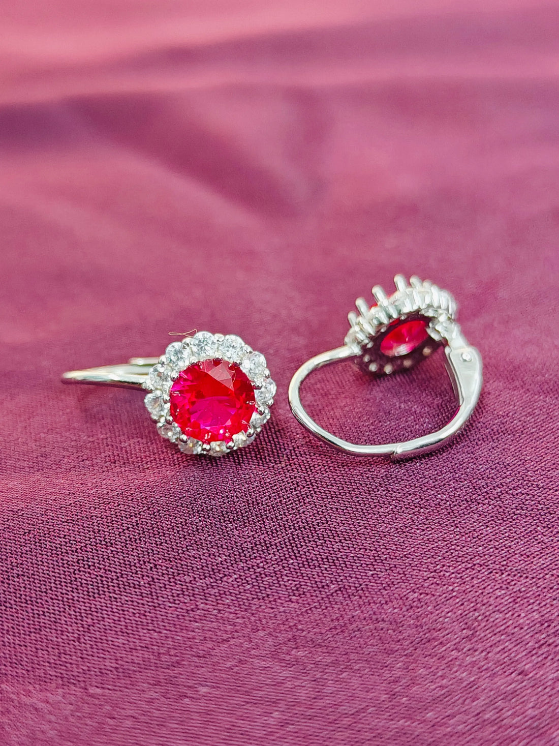 Two silver rings with red gemstones on a pink fabric background