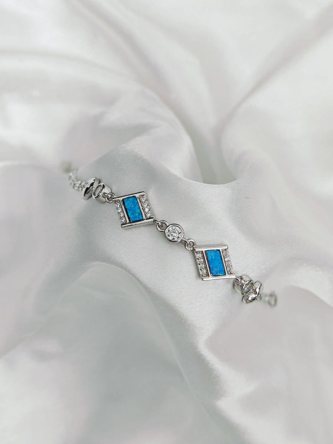 Silver bracelet with blue gemstones on a white fabric background