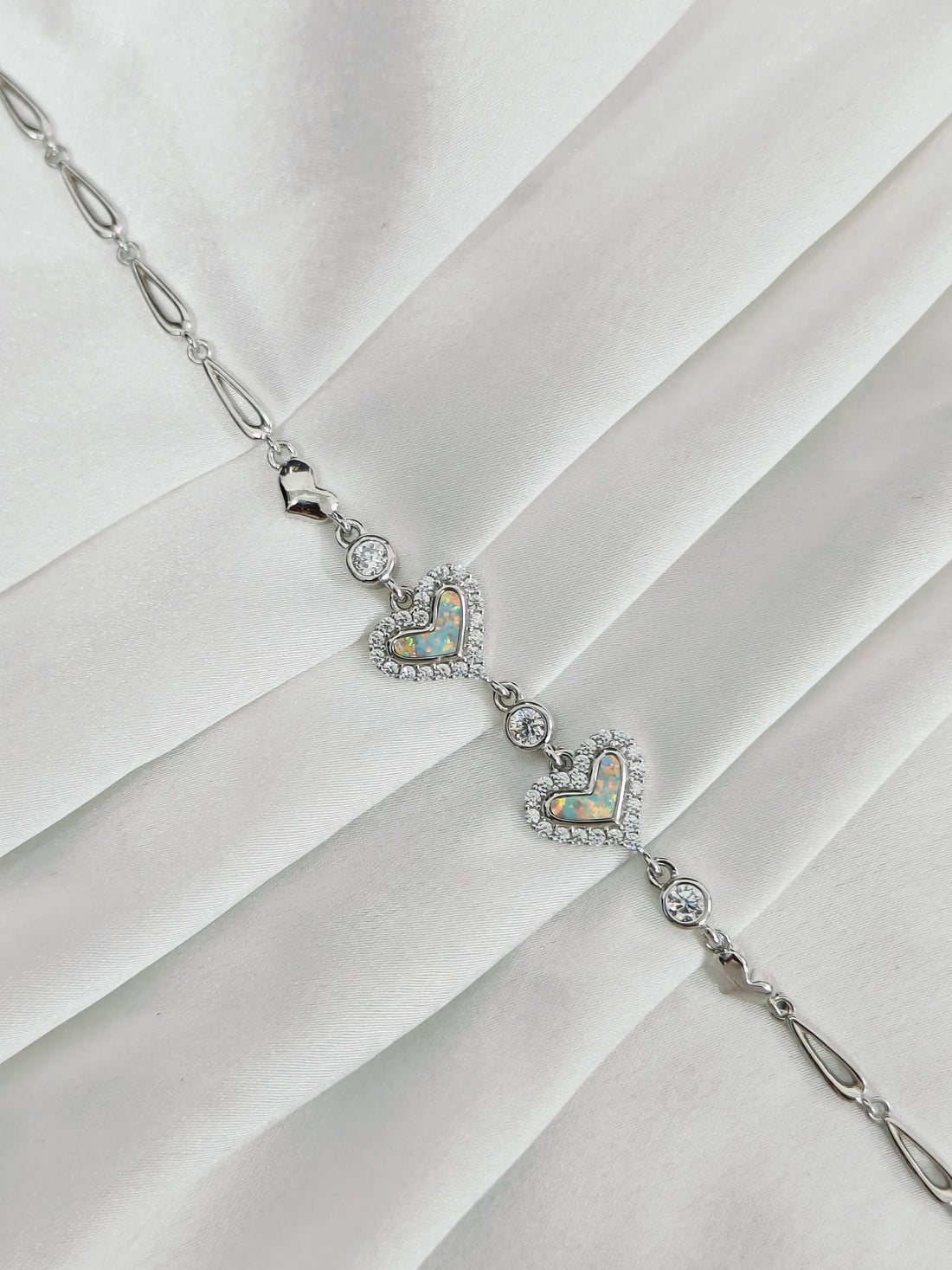 Silver necklace with heart-shaped opalite pendants on a white fabric background