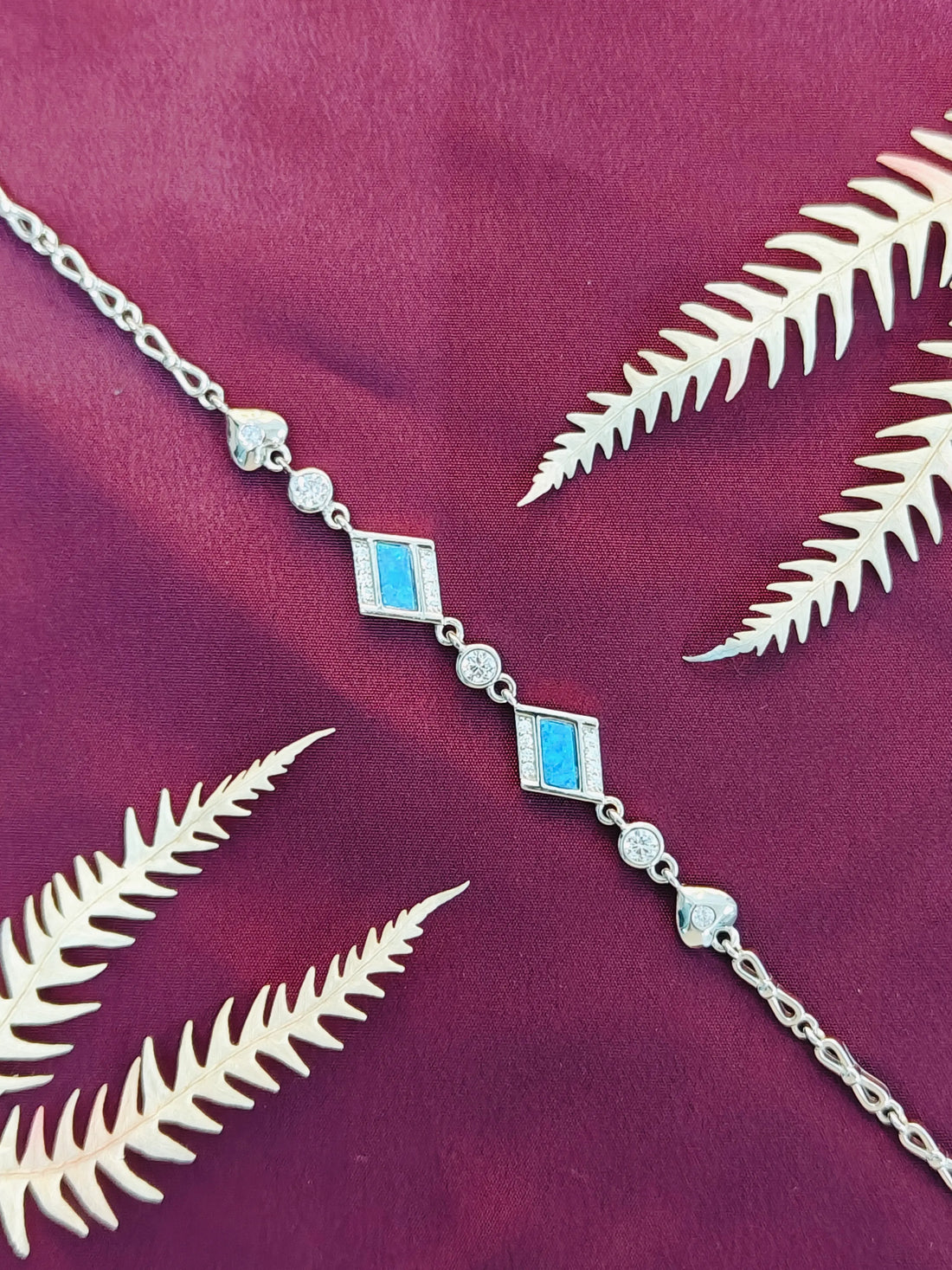 Silver chain necklace with blue accents on a purple fabric background with white leaves.