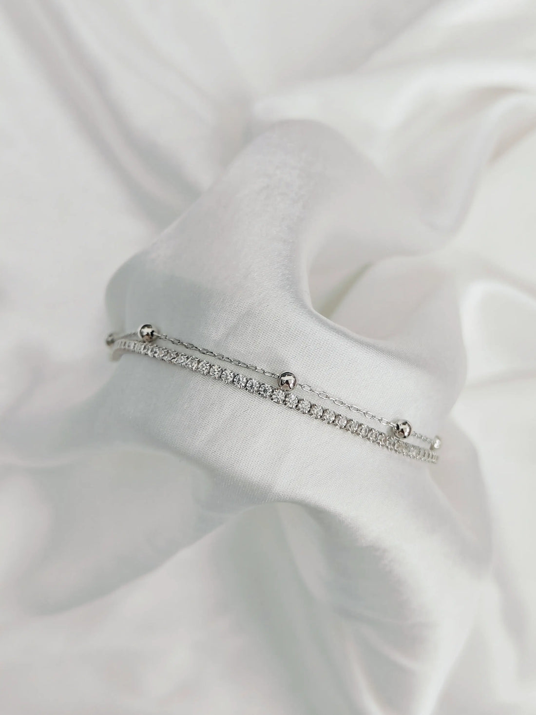 Silver bracelet with small stones on a white fabric background