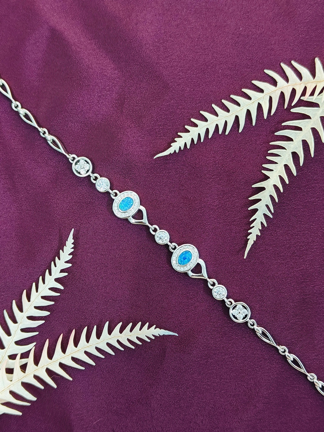 Silver anklet with blue stones on a purple fabric background with white leaves
