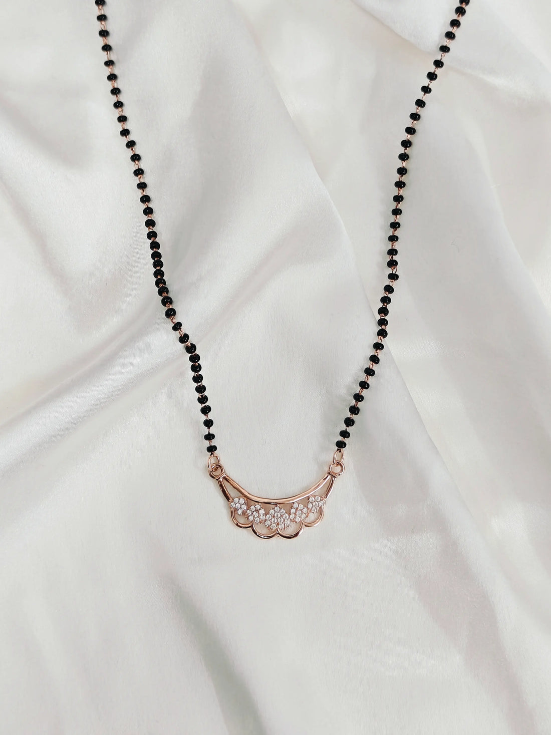 Necklace with black beads and a rose gold pendant on a white fabric background