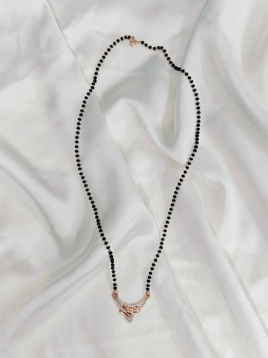 Black beaded necklace with a rose gold clasp on a white fabric background
