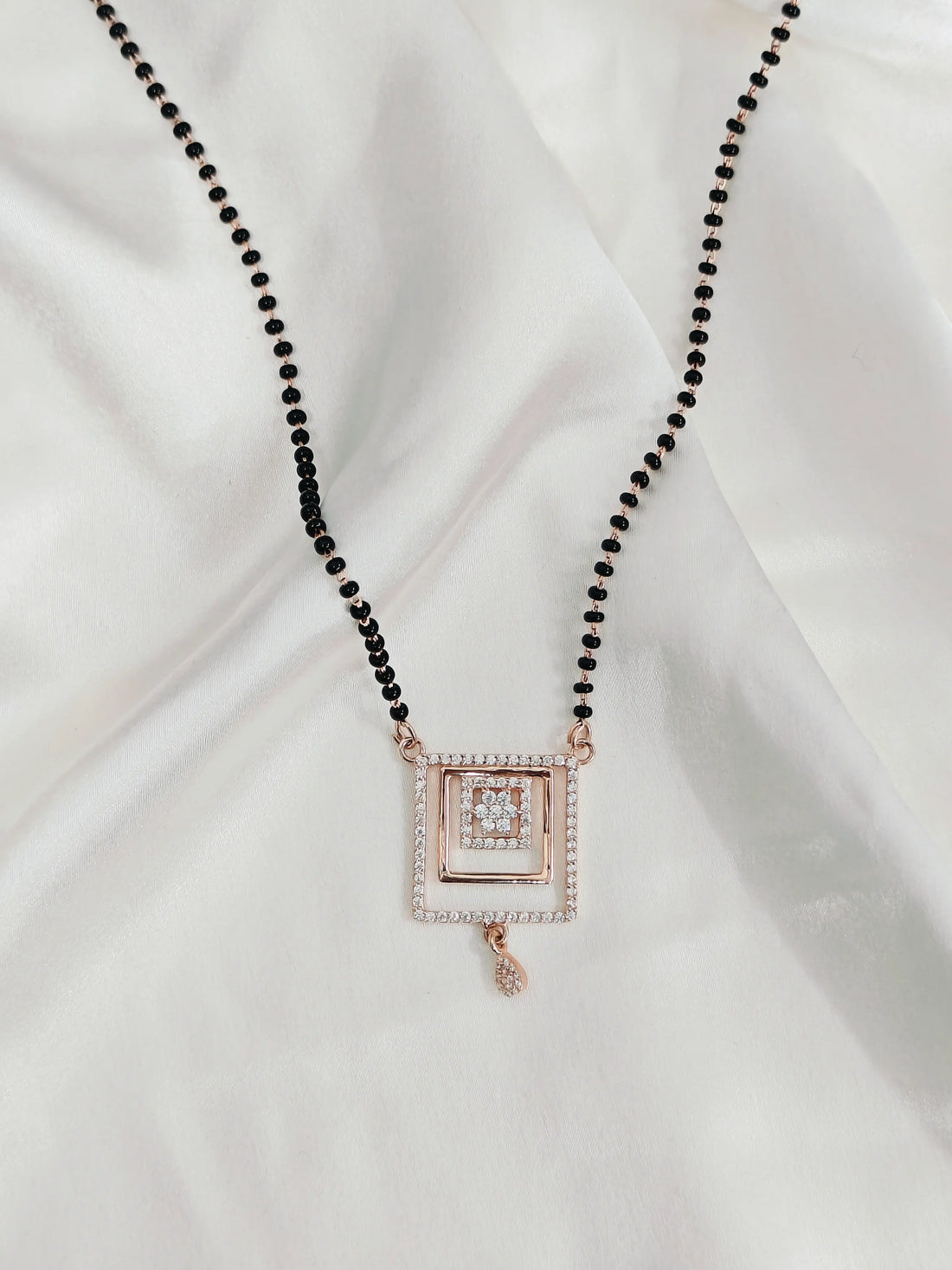 Necklace with black beads and a square pendant on a white fabric background