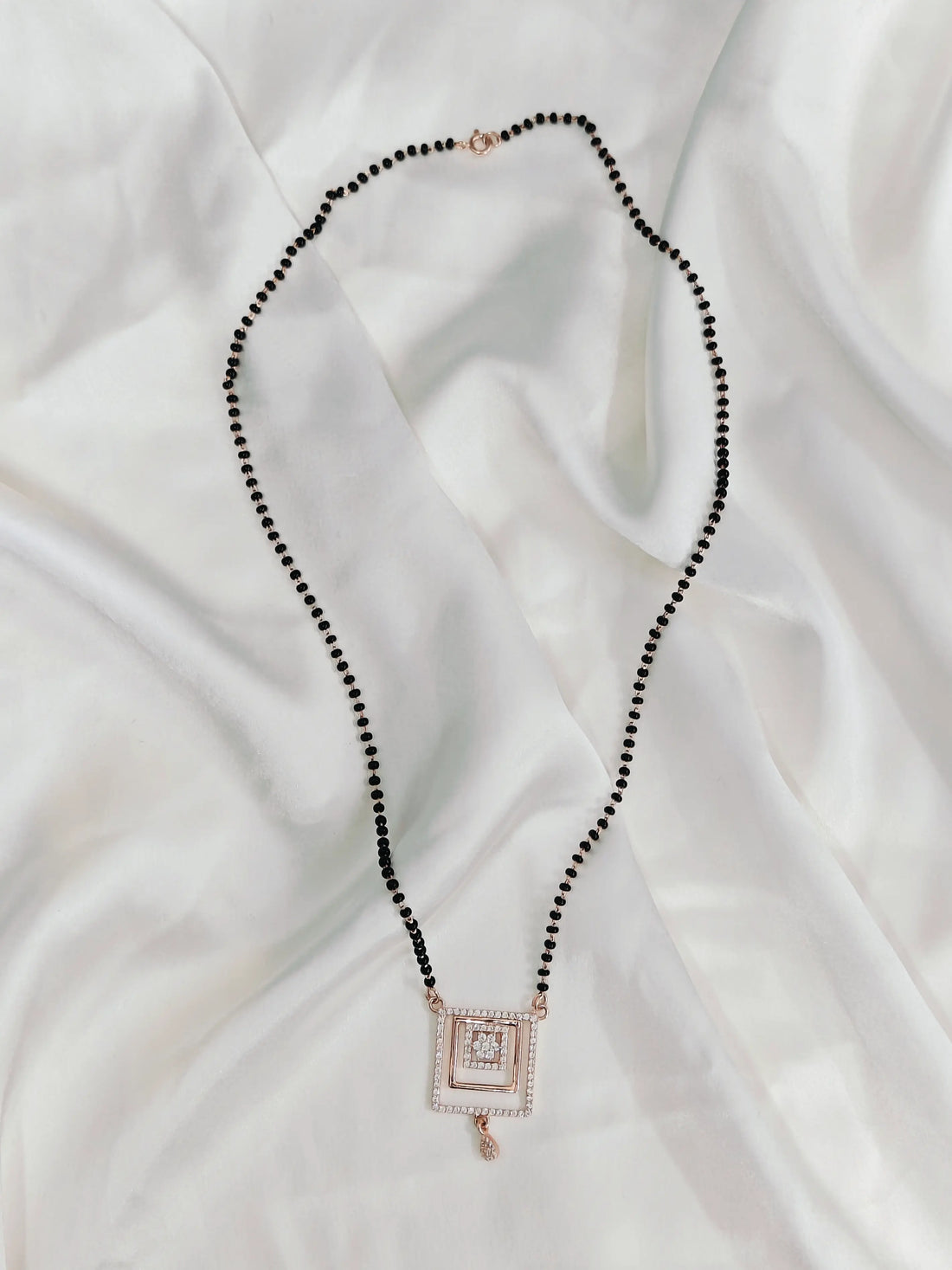 Necklace with black beads and a square pendant on a white fabric background