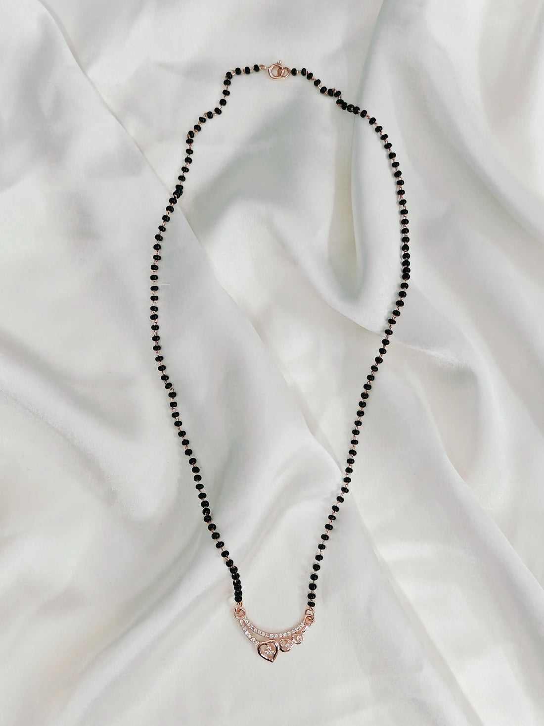 Necklace with black beads and a rose gold clasp on a white fabric background