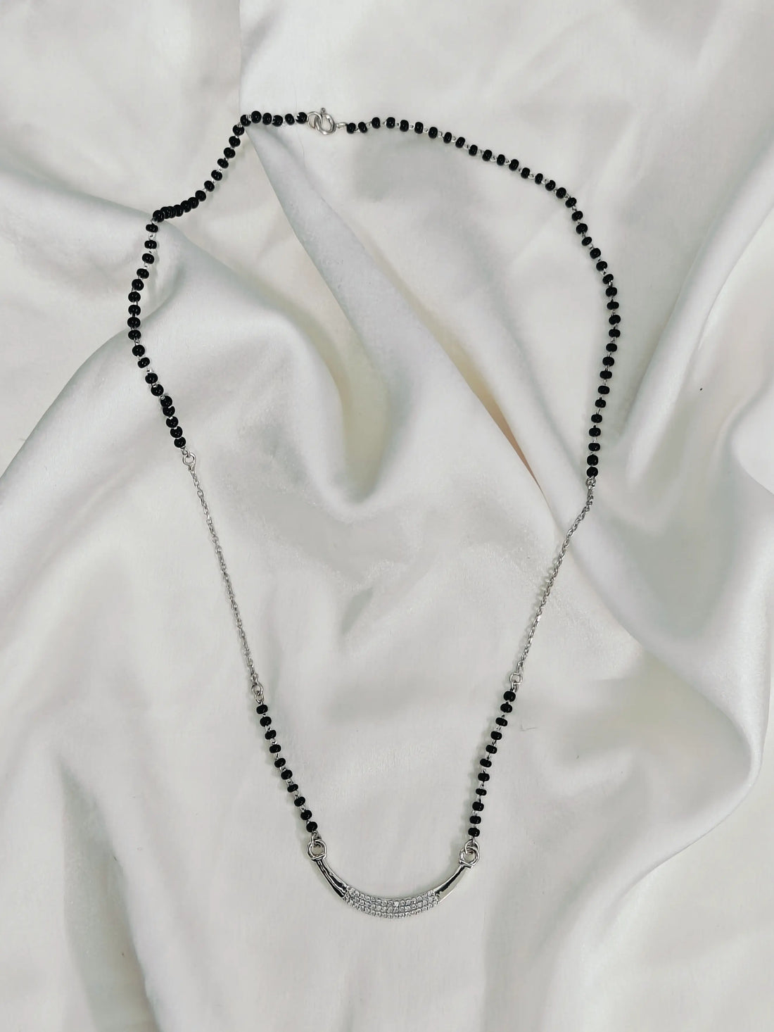 Necklace with black beads and silver clasp on a white fabric background