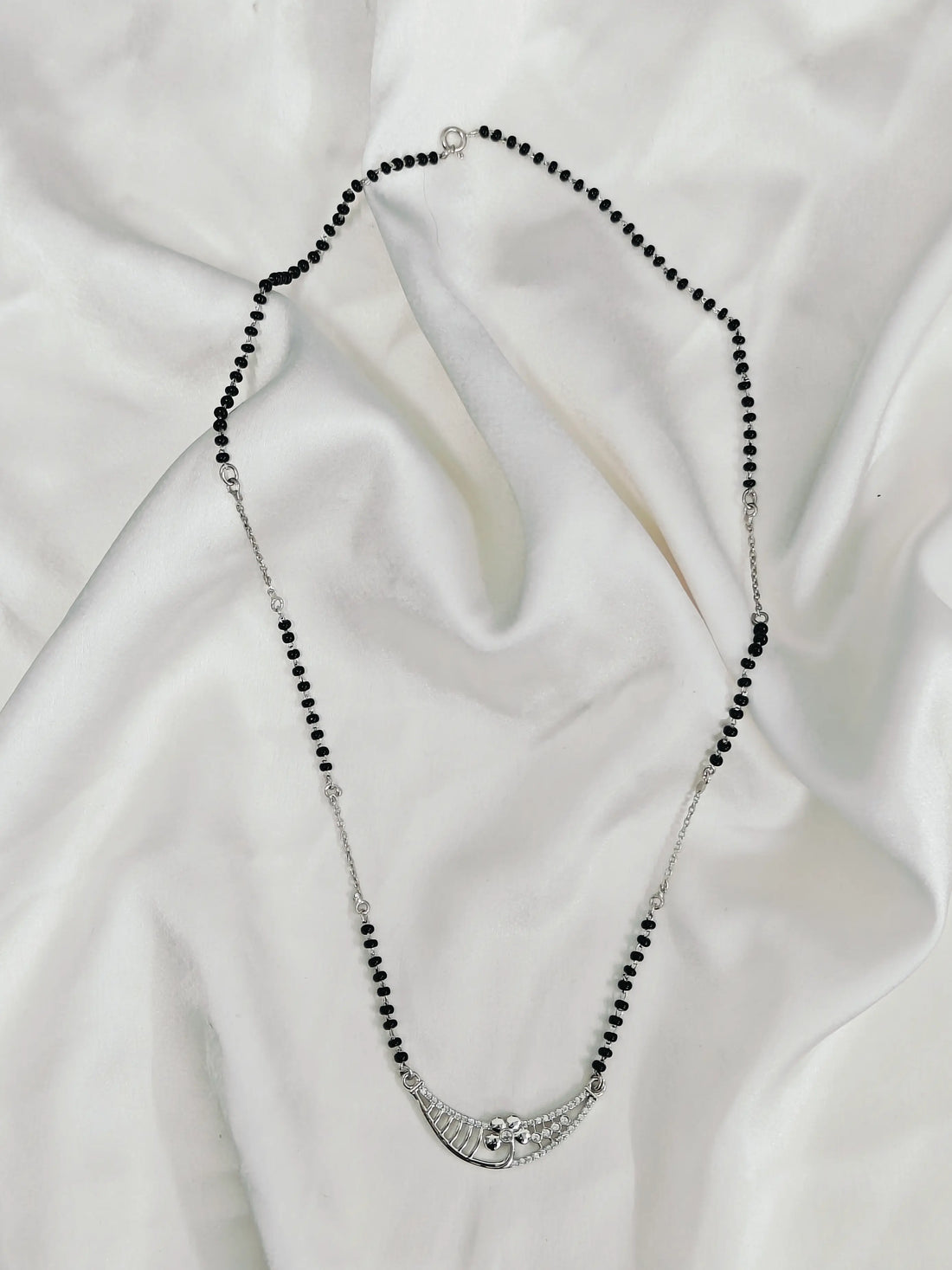 Necklace with black beads and silver clasp on a white fabric background