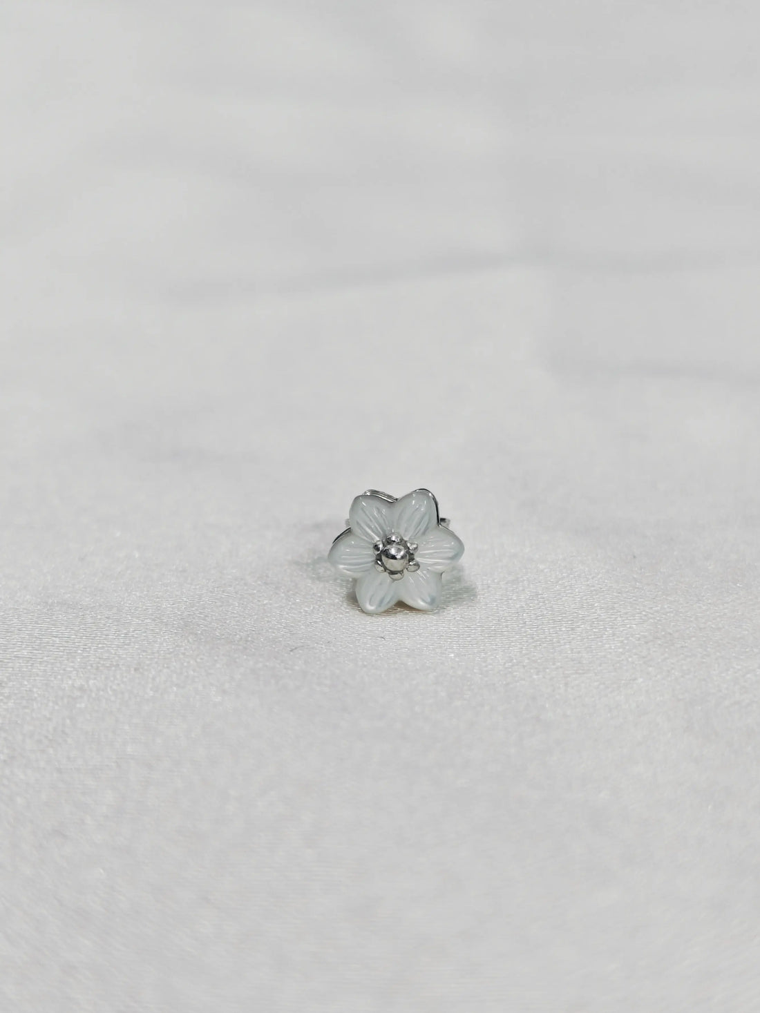 Silver flower-shaped earring on a light gray background