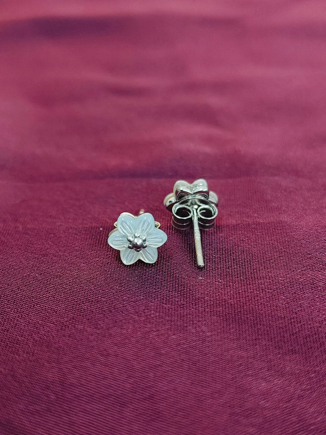 Silver flower-shaped earring and straight post earring on a purple fabric background