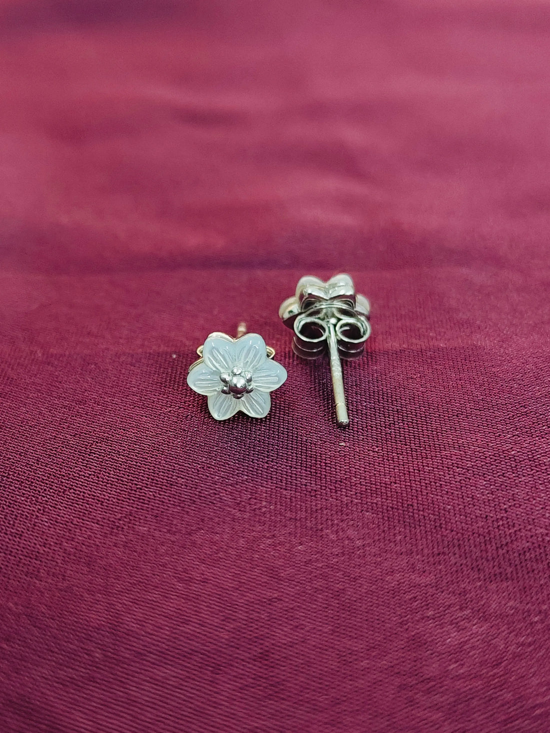 Silver flower-shaped earrings on a maroon fabric background