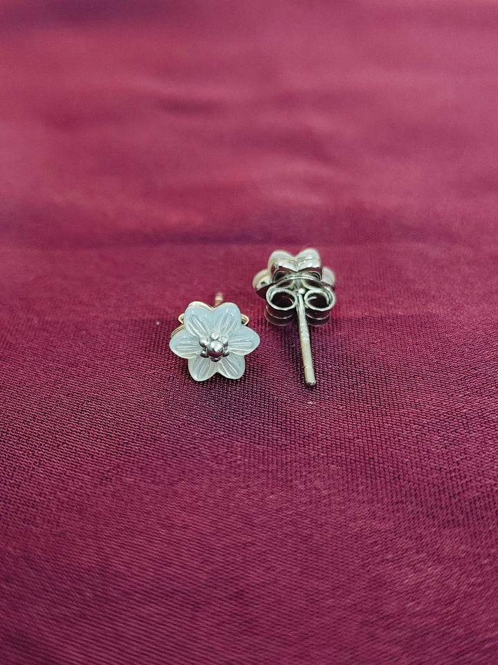 Silver flower-shaped earrings on a maroon fabric background