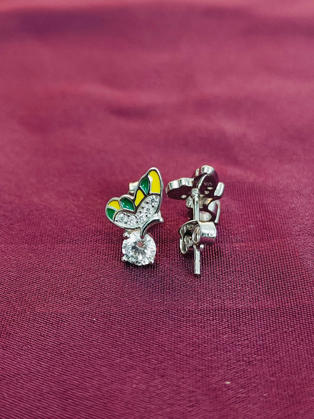 Butterfly-shaped earrings with gemstones on a maroon fabric background