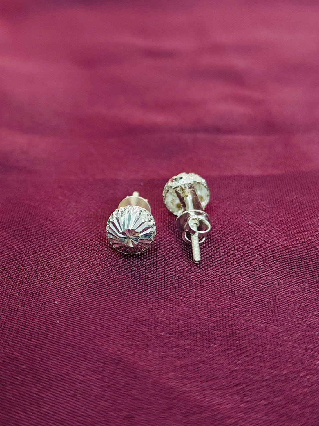Silver stud earrings on a maroon fabric background