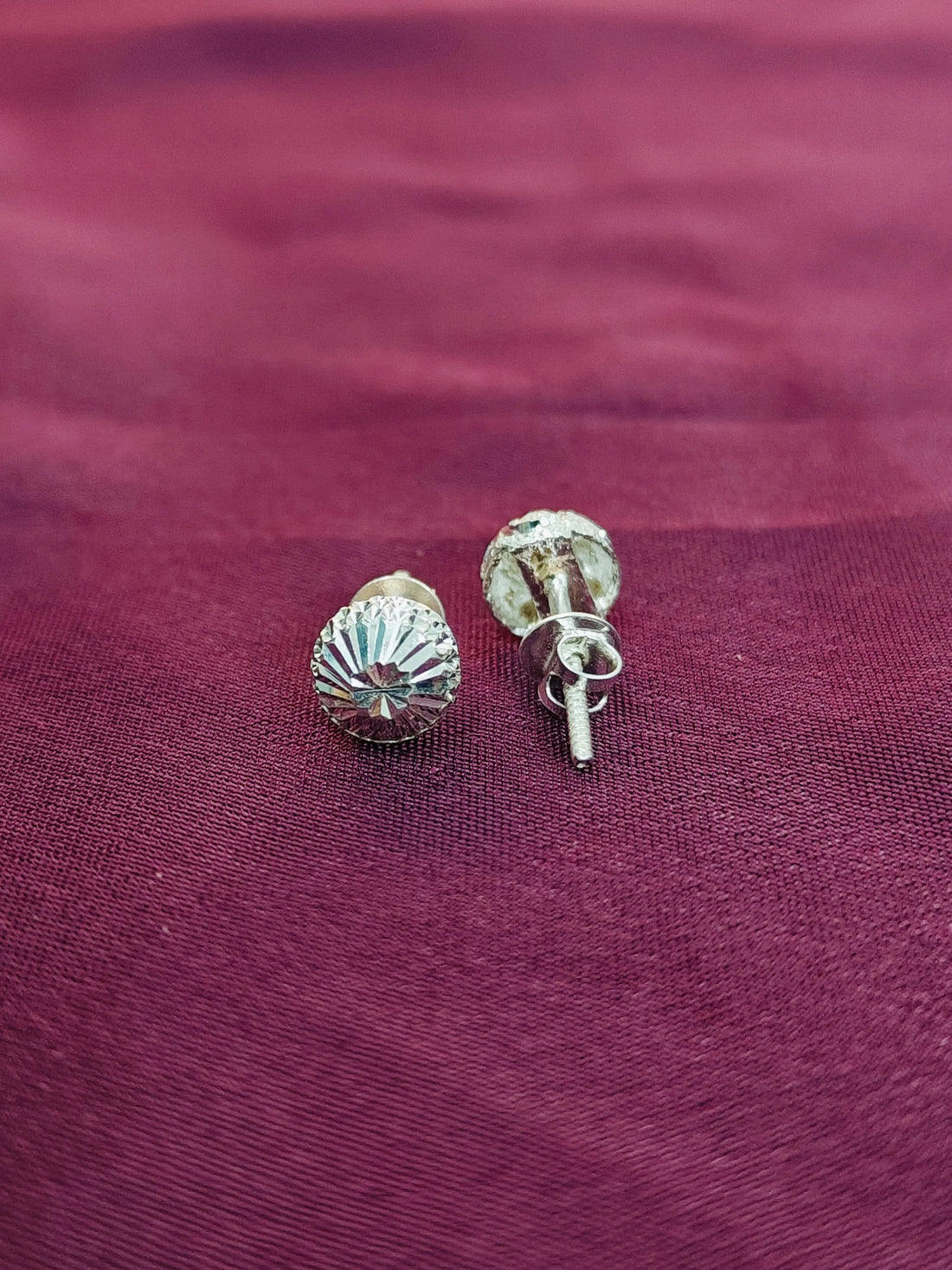 Silver shell-shaped earrings on a maroon fabric background