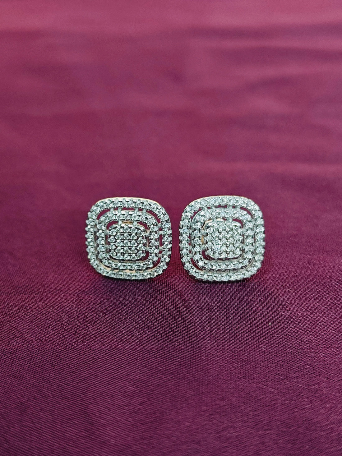 Pair of silver square earrings on a purple fabric background