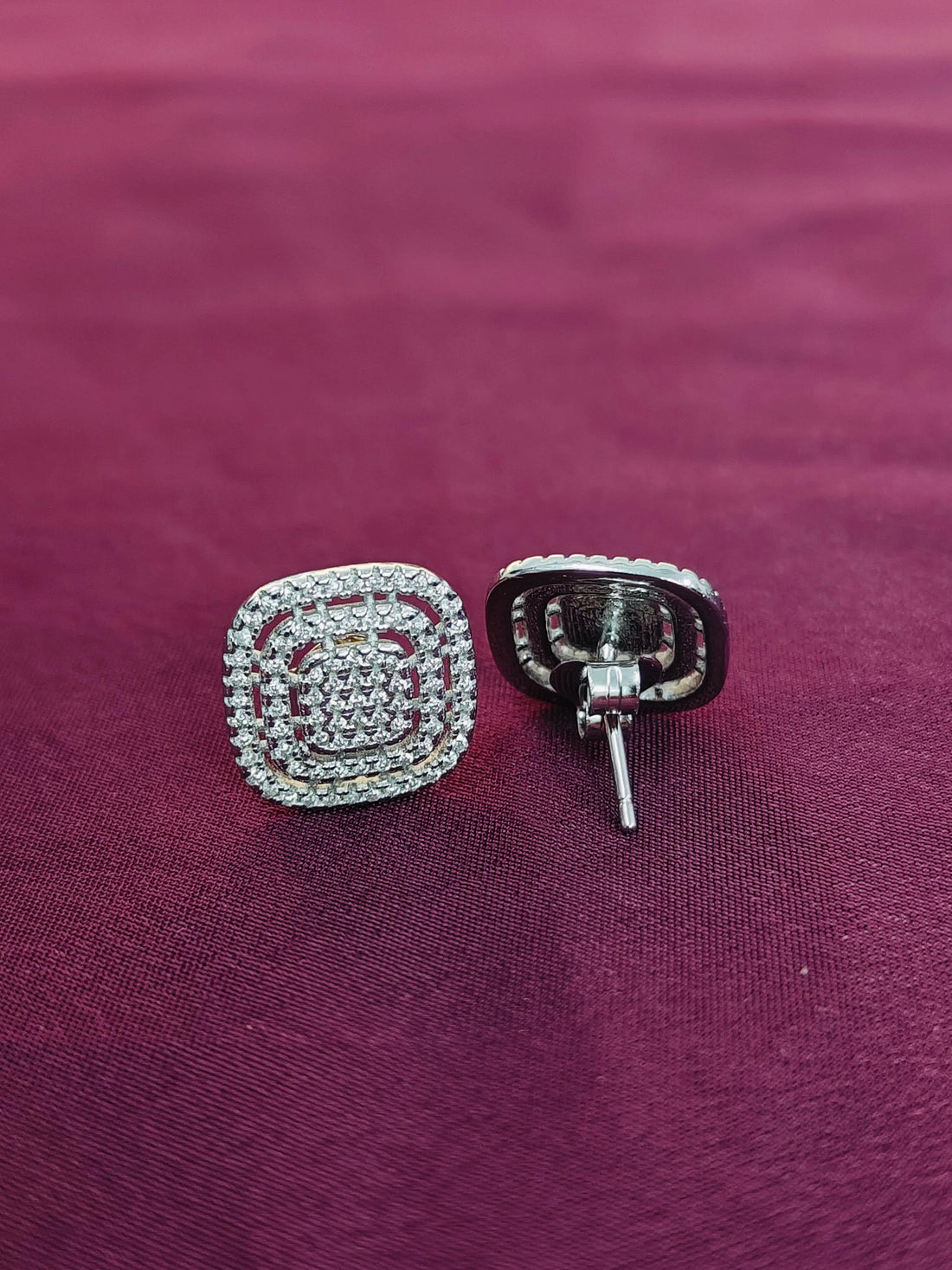 Silver square-shaped earrings on a purple fabric background