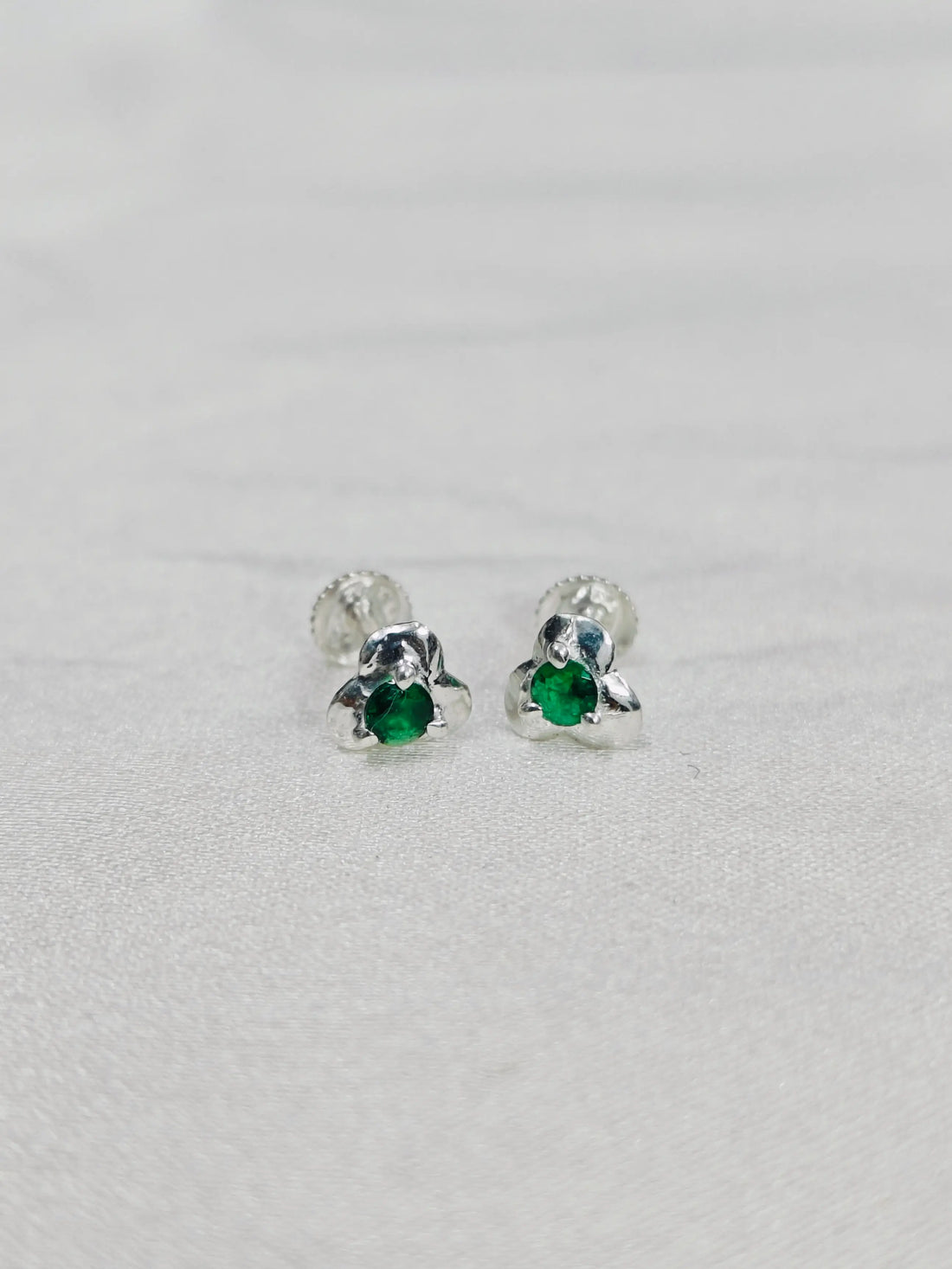 Silver earrings with green gemstones on a light gray background