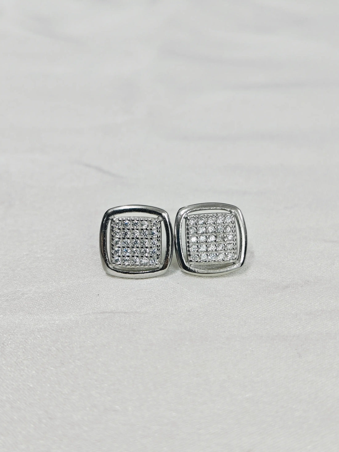 Pair of silver square earrings with clear stones on a light gray background