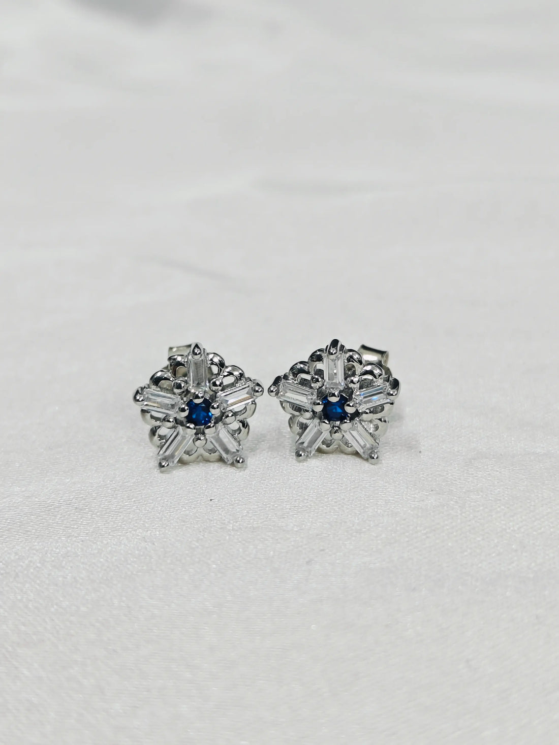 Pair of silver earrings with blue gemstones on a light gray background