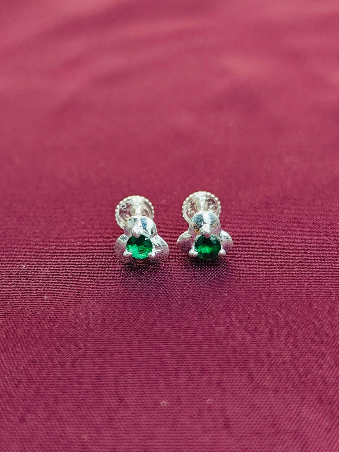 Silver earrings with green gemstones on a maroon fabric background