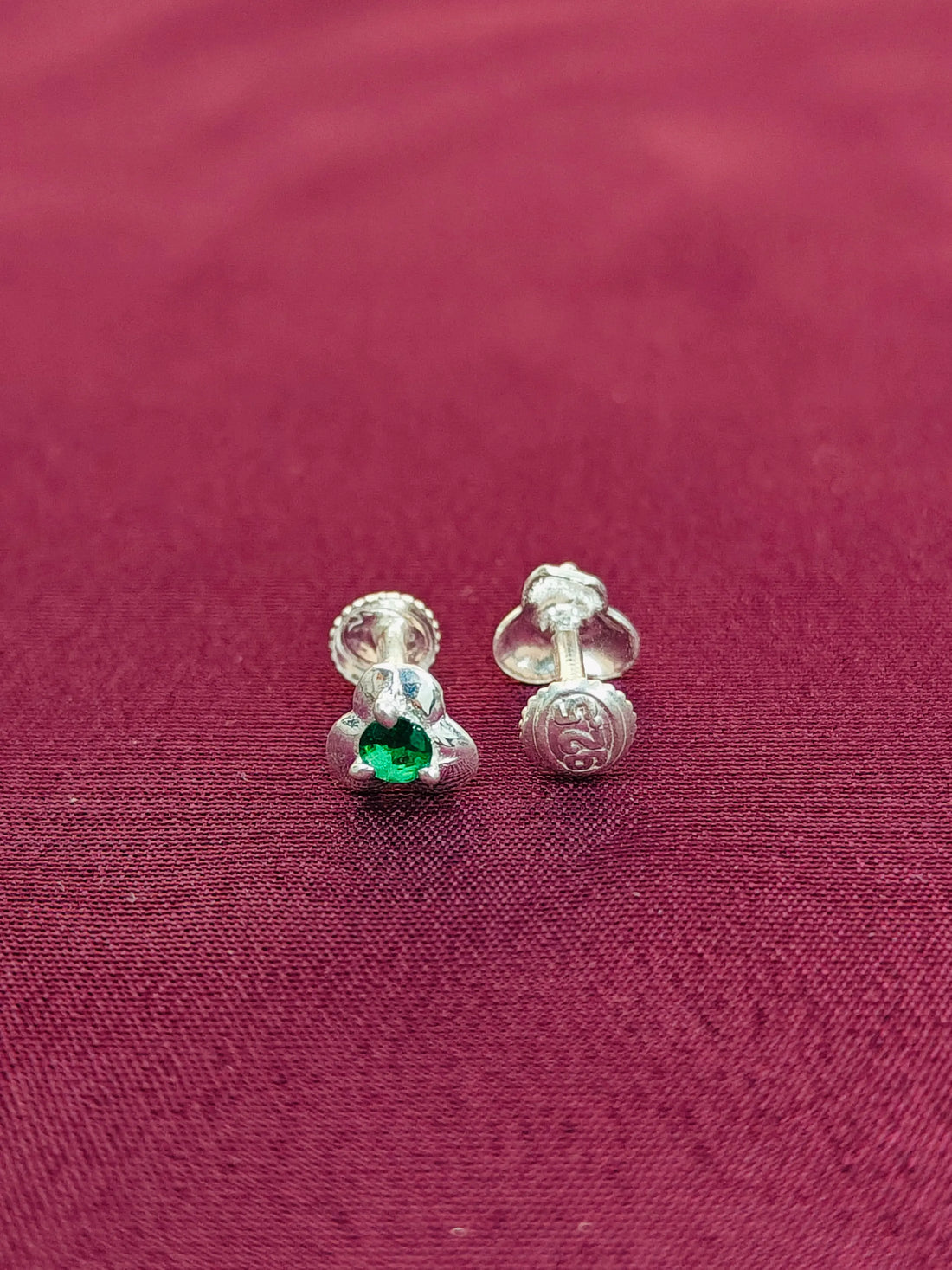 Silver earrings with a green gemstone on a red fabric background