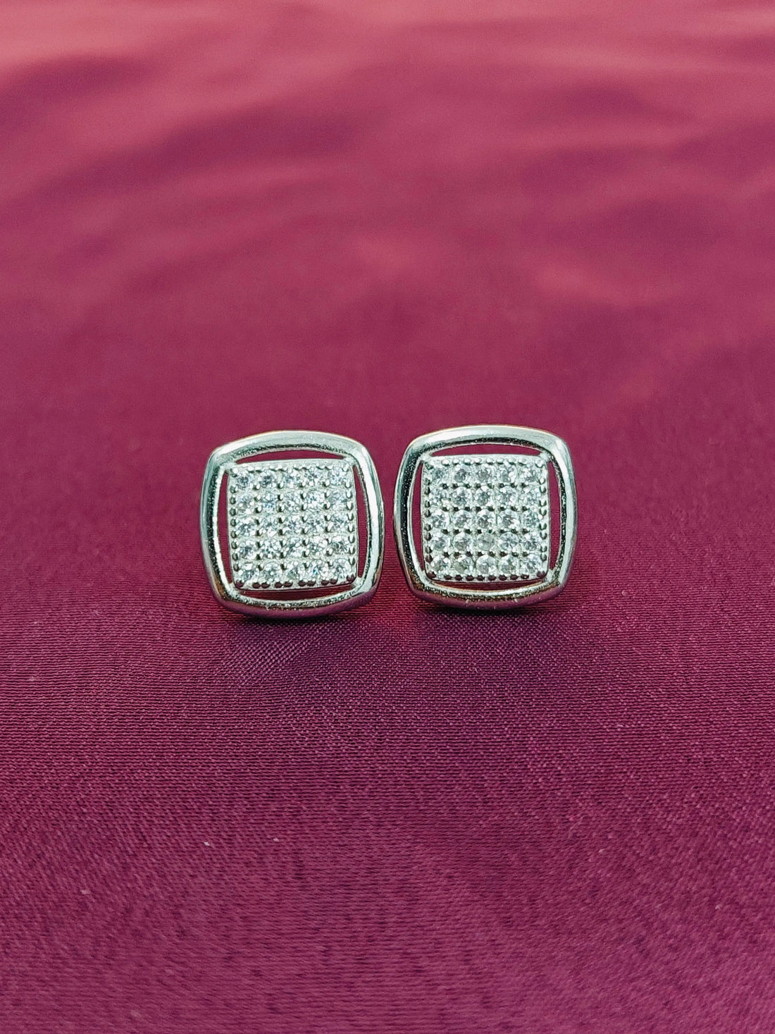 Pair of silver square earrings with clear stones on a purple fabric background