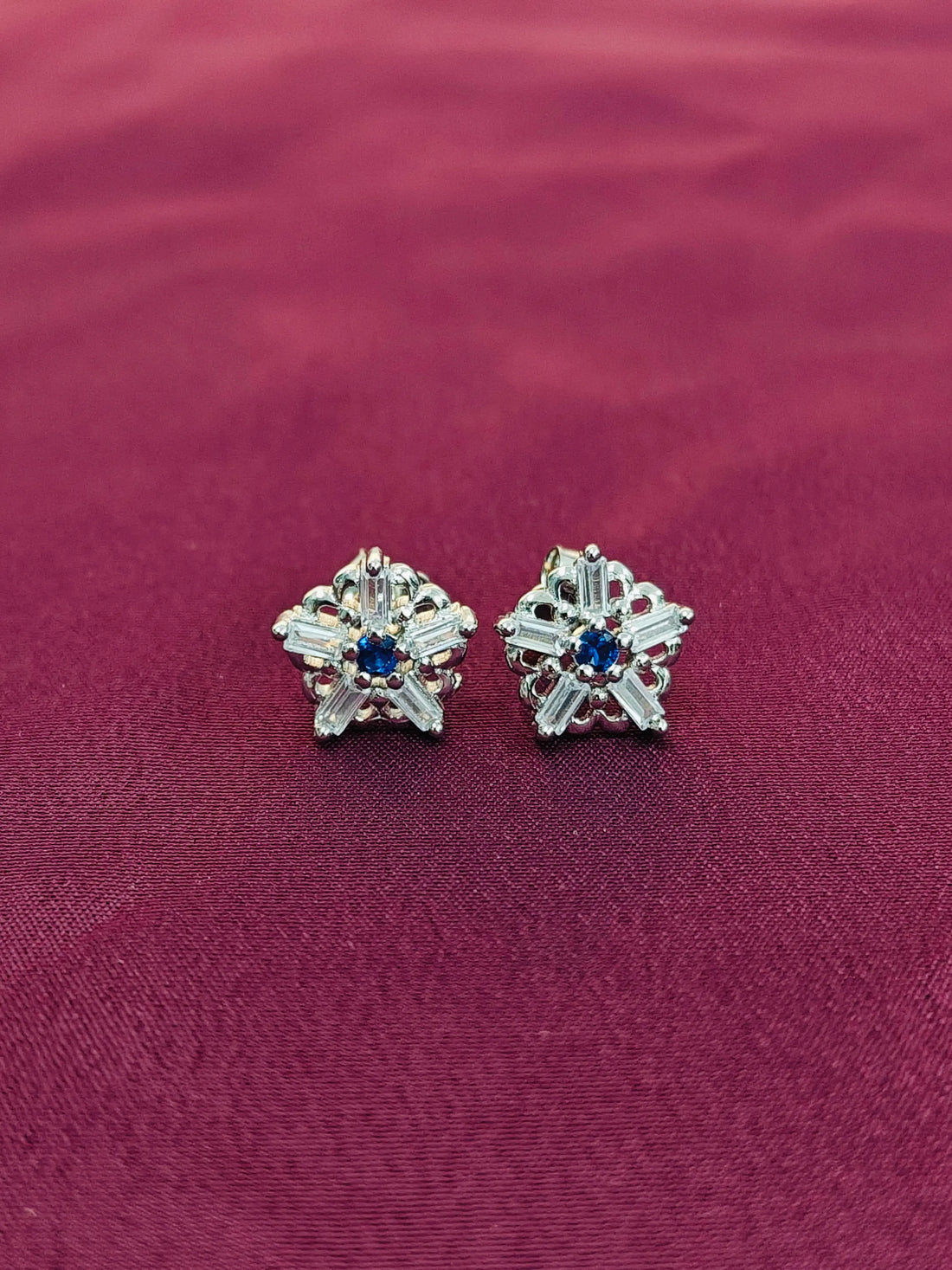 Star-shaped earrings with gemstones on a red fabric background