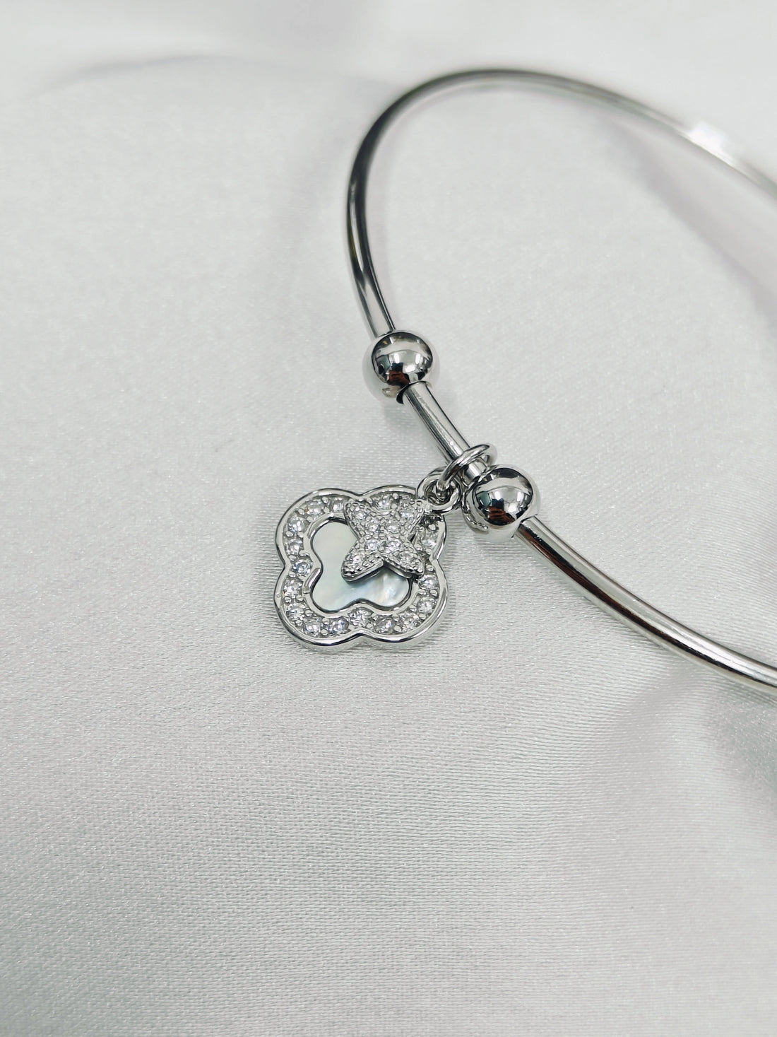 Silver bangle with a heart-shaped charm on a light gray background